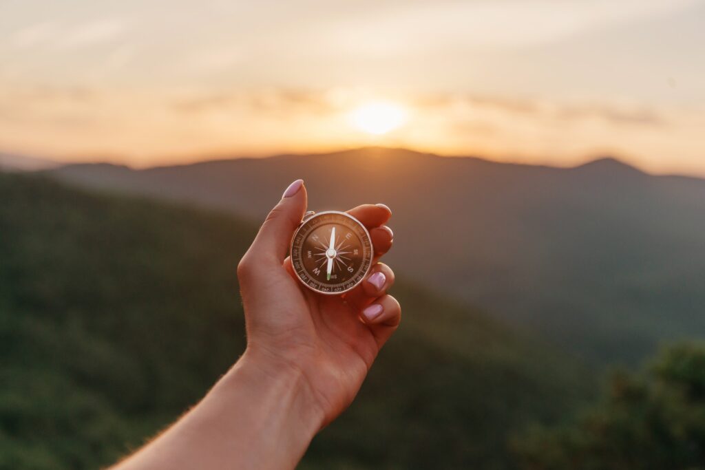 Female hand with compass in summer mountains at sunrise, pov