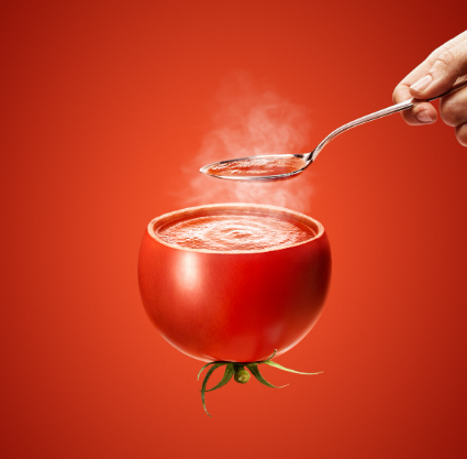 upside down tomato with soup inside with hand spooning some.