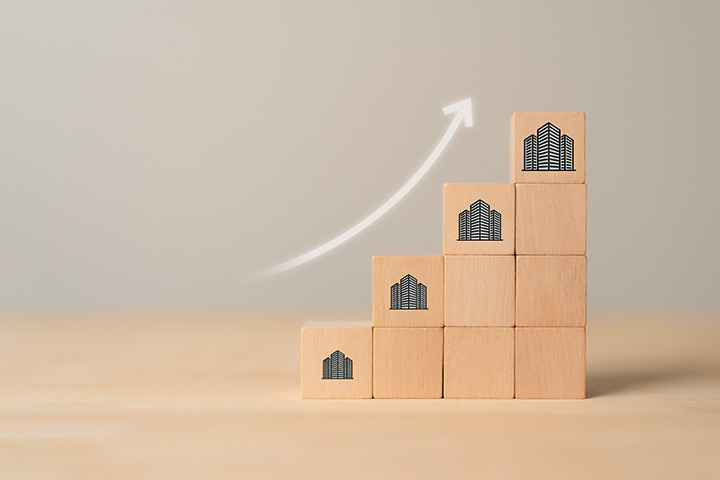 Four stacks of blocks where each is larger than the next with an arrow pointing diagonally up from the shortest stack to indicate growth
