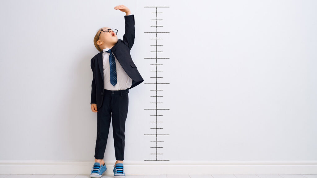 Young Boy in a suit standing next to a growth chart