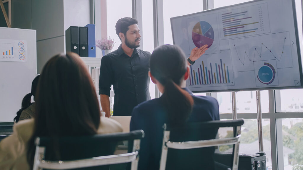 Man explaining data on monitor to meeting room