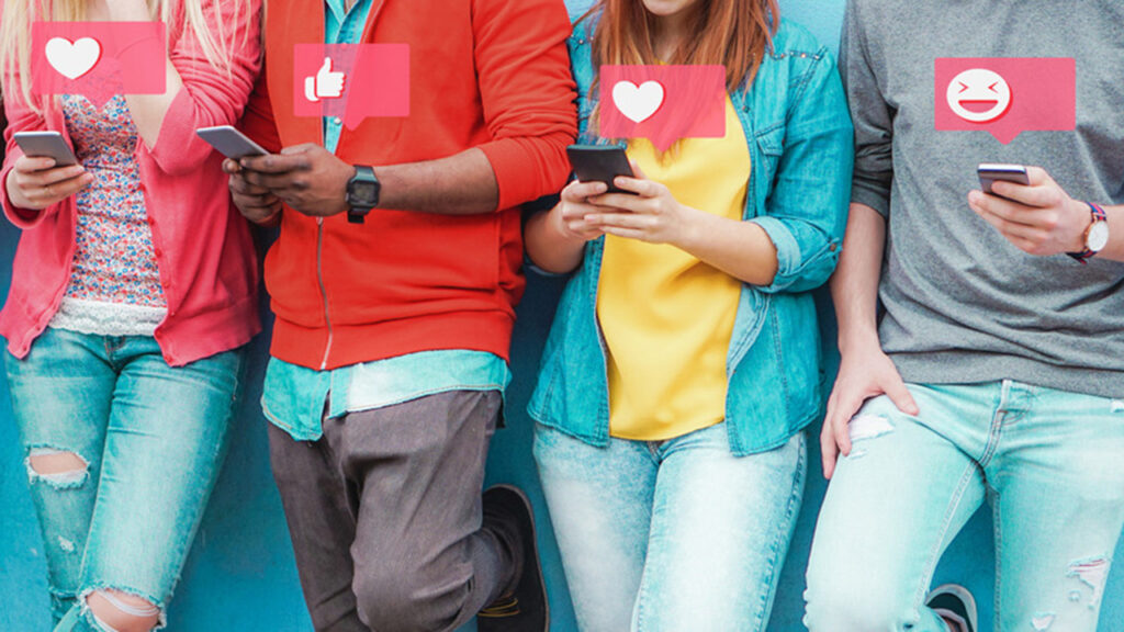 Image of four people leaning against the wall looking at their cellphones with illustration chat bubbles with different emojis hovering over the phones